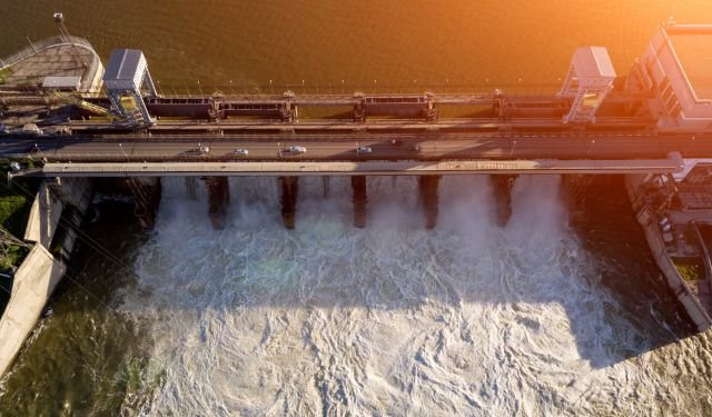 hydropower dam in the sunshine with cars on the rods on the dam
